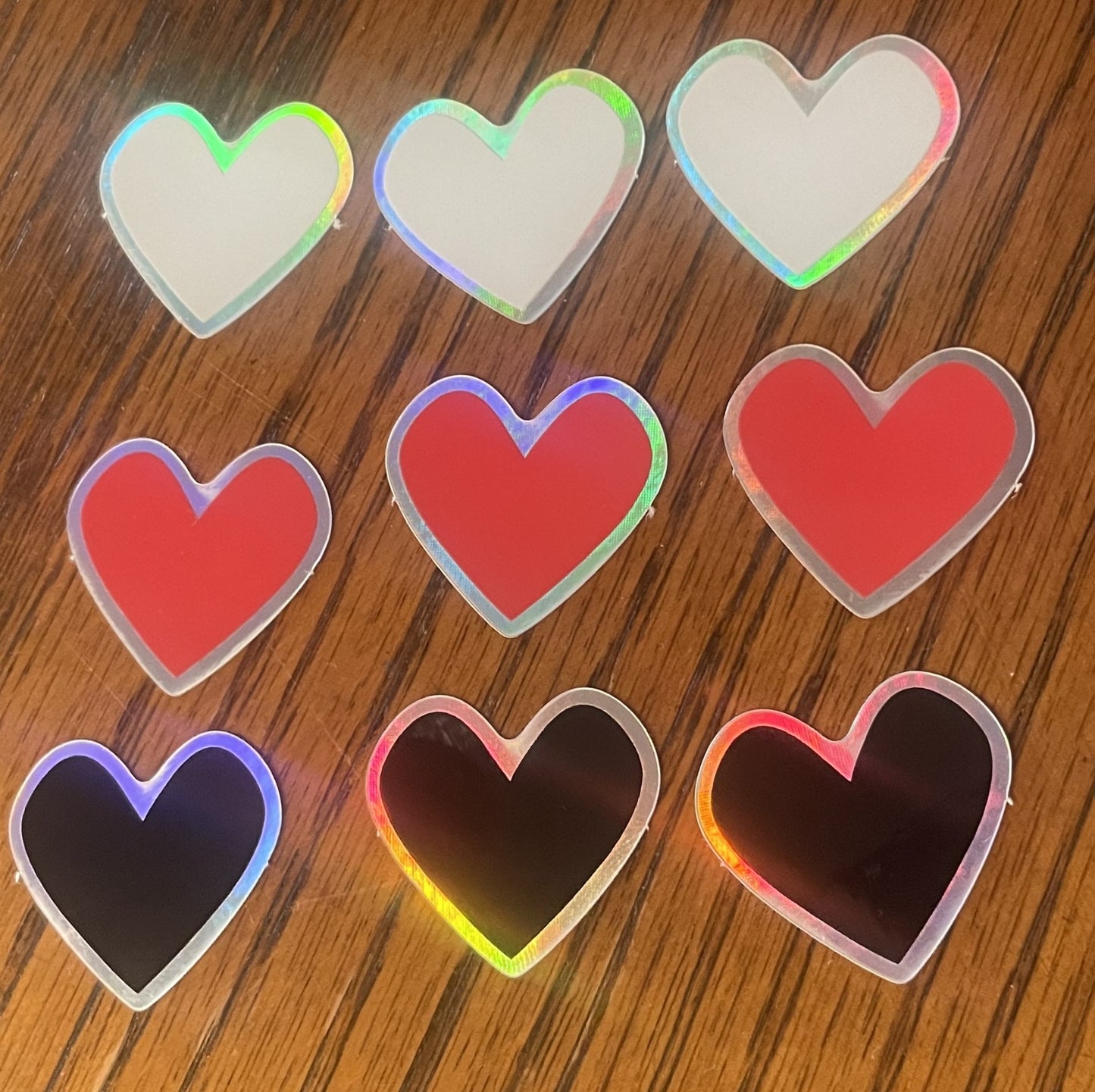 3 holographic black heart stickers, 3 holographic red heart stickers, and 3 holographic white heart stickers shown. Each sticker is 1x1 inch, with holographic dye cut edges.